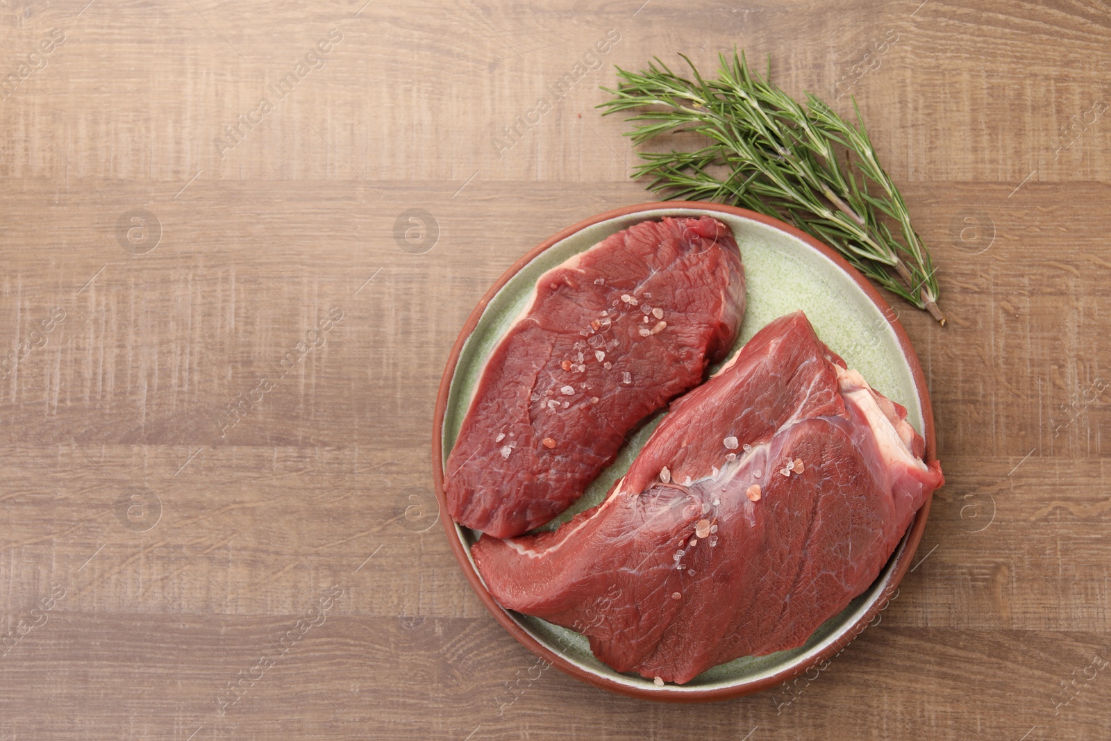 Photo of Pieces of raw beef meat with spices and rosemary on wooden table, flat lay. Space for text