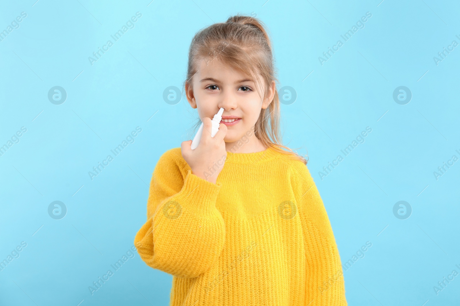 Photo of Sick little girl using nasal spray on light blue background