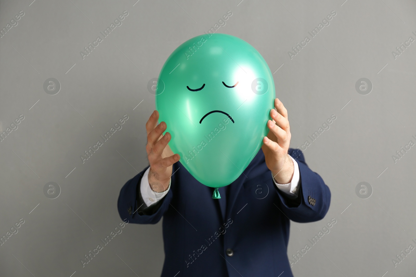 Photo of Man holding green air balloon with drawn sad face on grey background