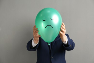 Photo of Man holding green air balloon with drawn sad face on grey background