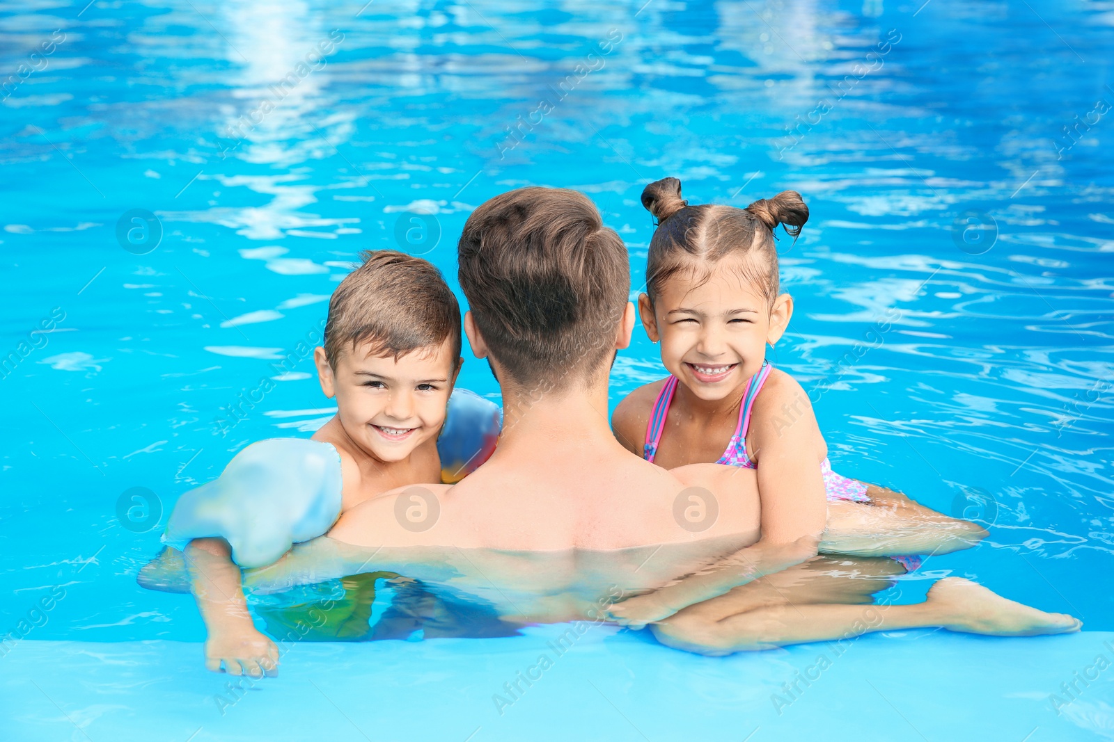 Photo of Young father with little children in swimming pool on sunny day