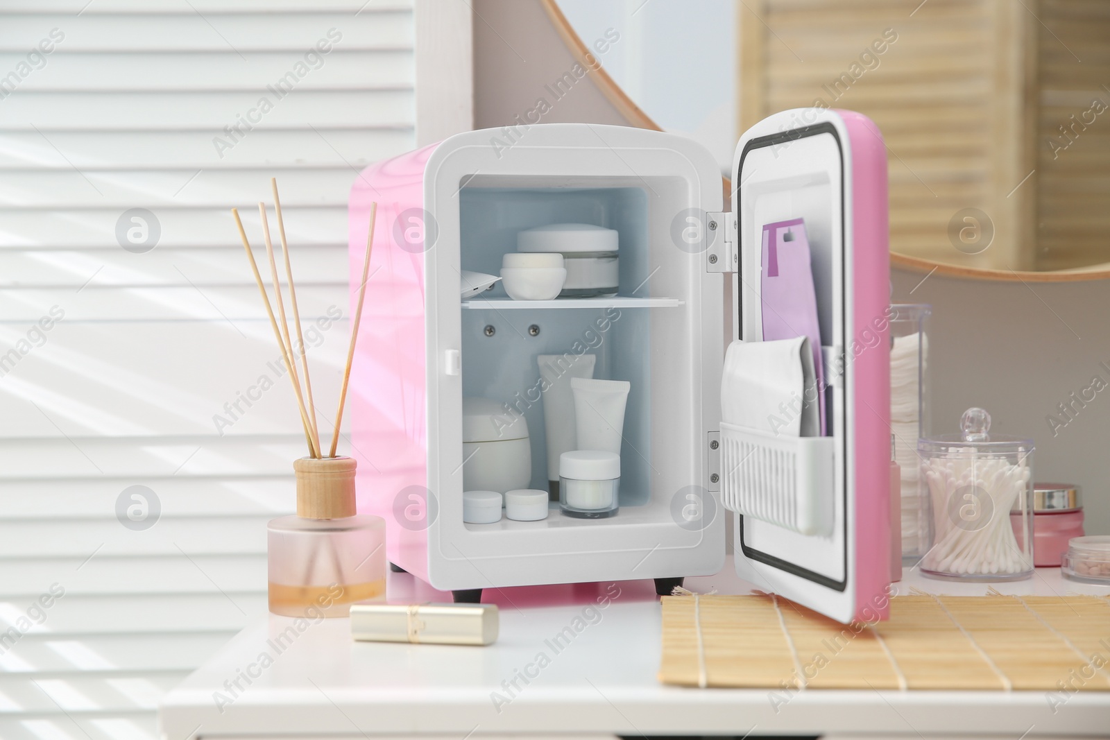 Photo of Cosmetics refrigerator and skin care products on white vanity table indoors