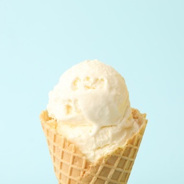 Delicious ice cream in waffle cone on light blue background, closeup