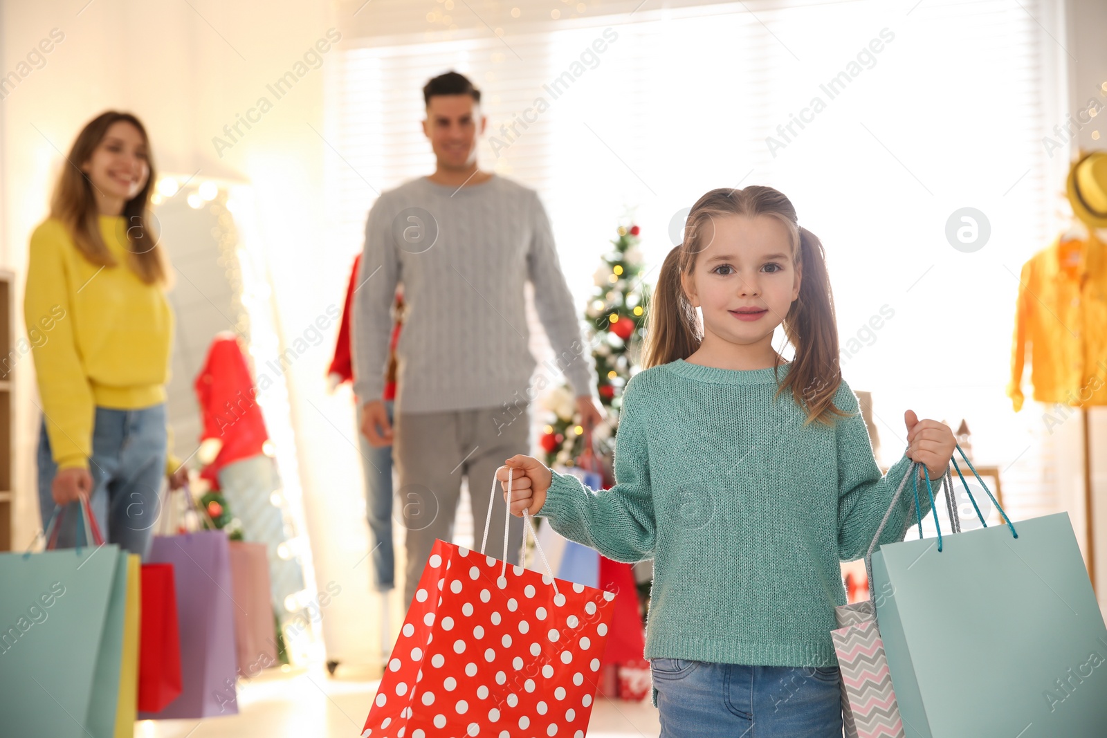 Photo of Little girl with bags near her parents in store. Family Christmas shopping