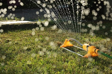 Photo of Automatic sprinkler watering green grass on sunny day outdoors. Irrigation system