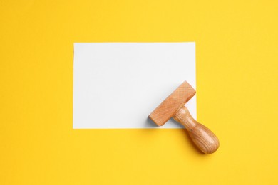 Photo of One wooden stamp tool and sheet of paper on yellow background, top view. Space for text