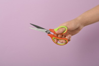 Photo of Woman holding office scissors on lilac background, closeup