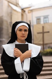 Young nun with Bible near building outdoors