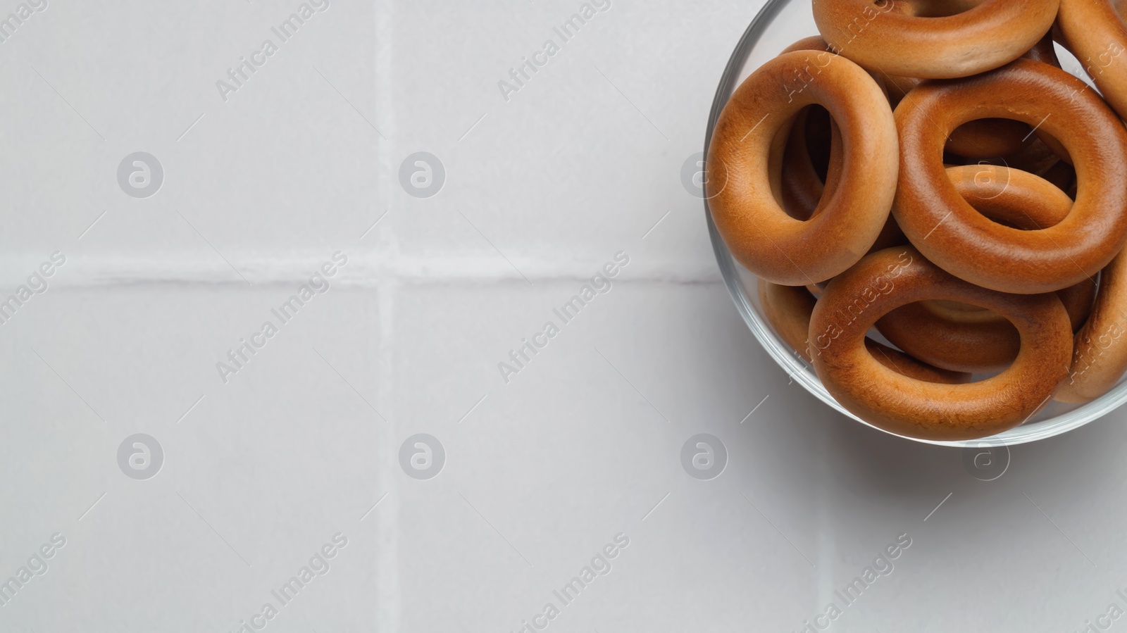 Photo of Bowl of tasty dry bagels (sushki) on white tiled table, top view. Space for text