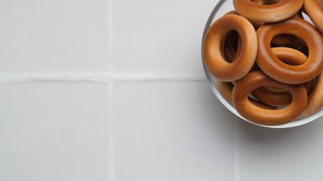 Photo of Bowl of tasty dry bagels (sushki) on white tiled table, top view. Space for text