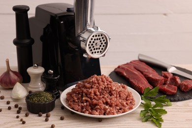 Photo of Electric meat grinder with beef, spices and parsley on white wooden table