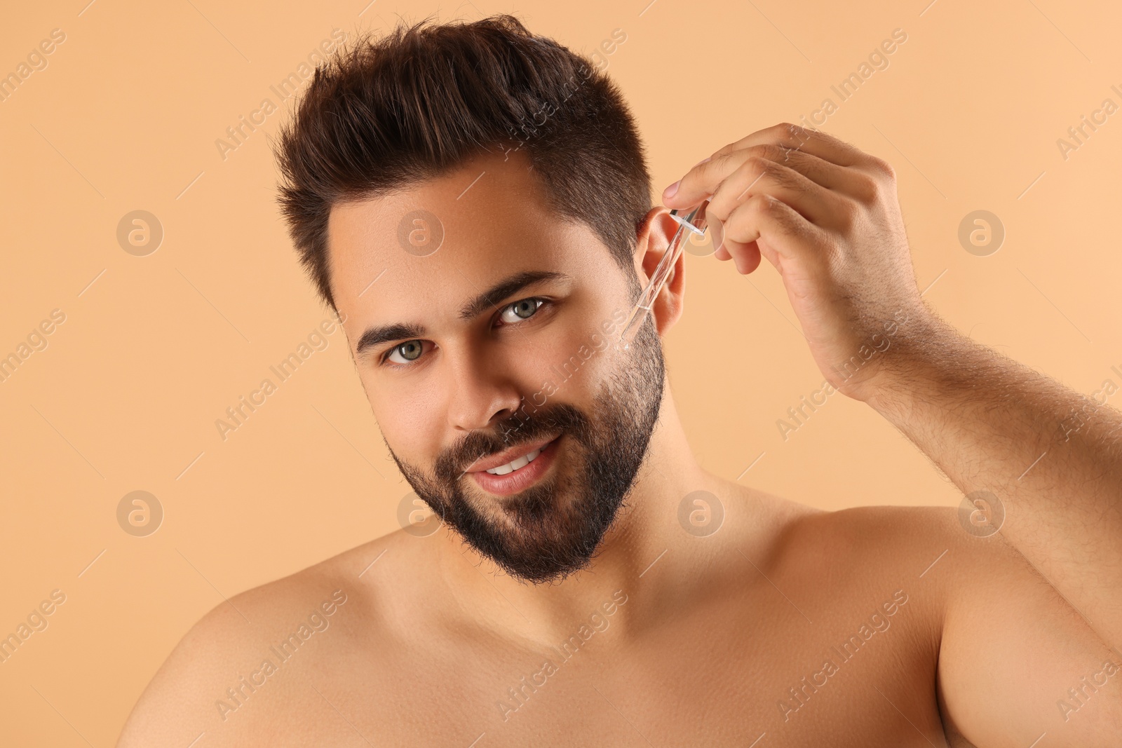 Photo of Handsome man applying cosmetic serum onto face on beige background