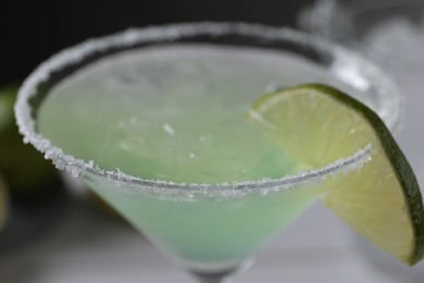 Delicious Margarita cocktail with ice cubes in glass and lime on table, closeup