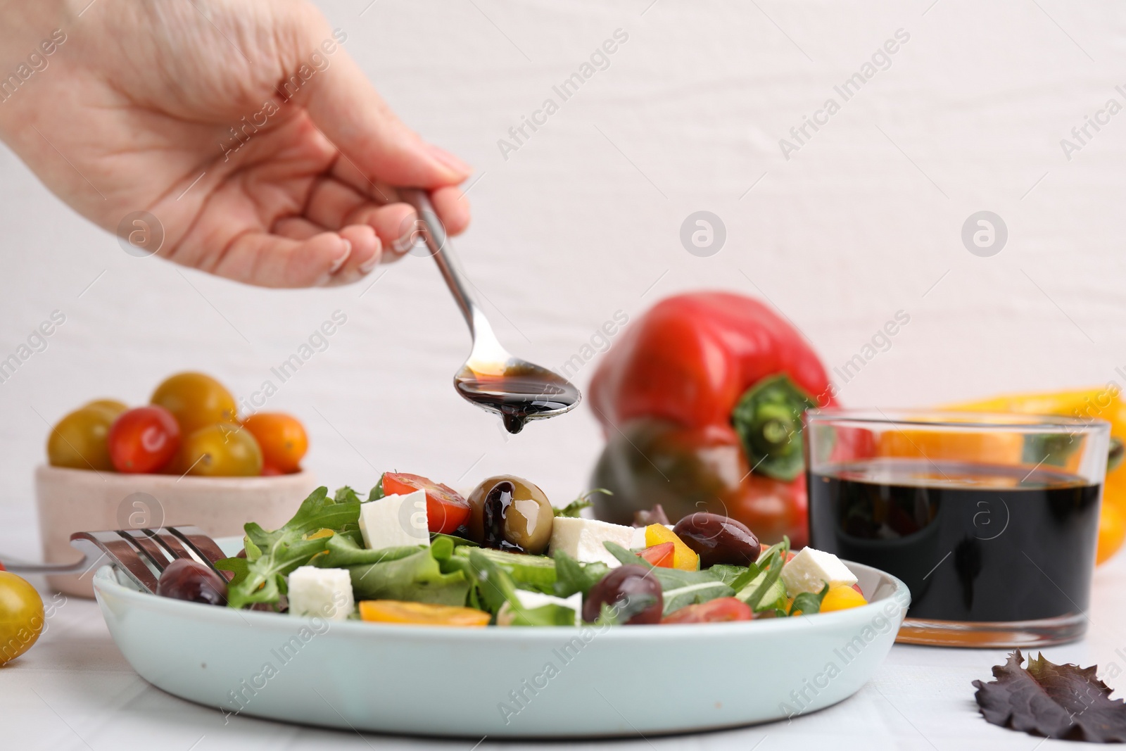 Photo of Woman pouring vinegar from spoon into plate with salad at white tiled table, closeup