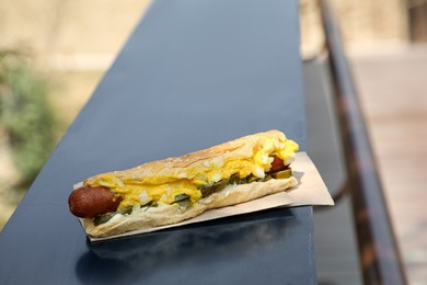 Photo of Fresh tasty hot dog with sauce on dark parapet outdoors