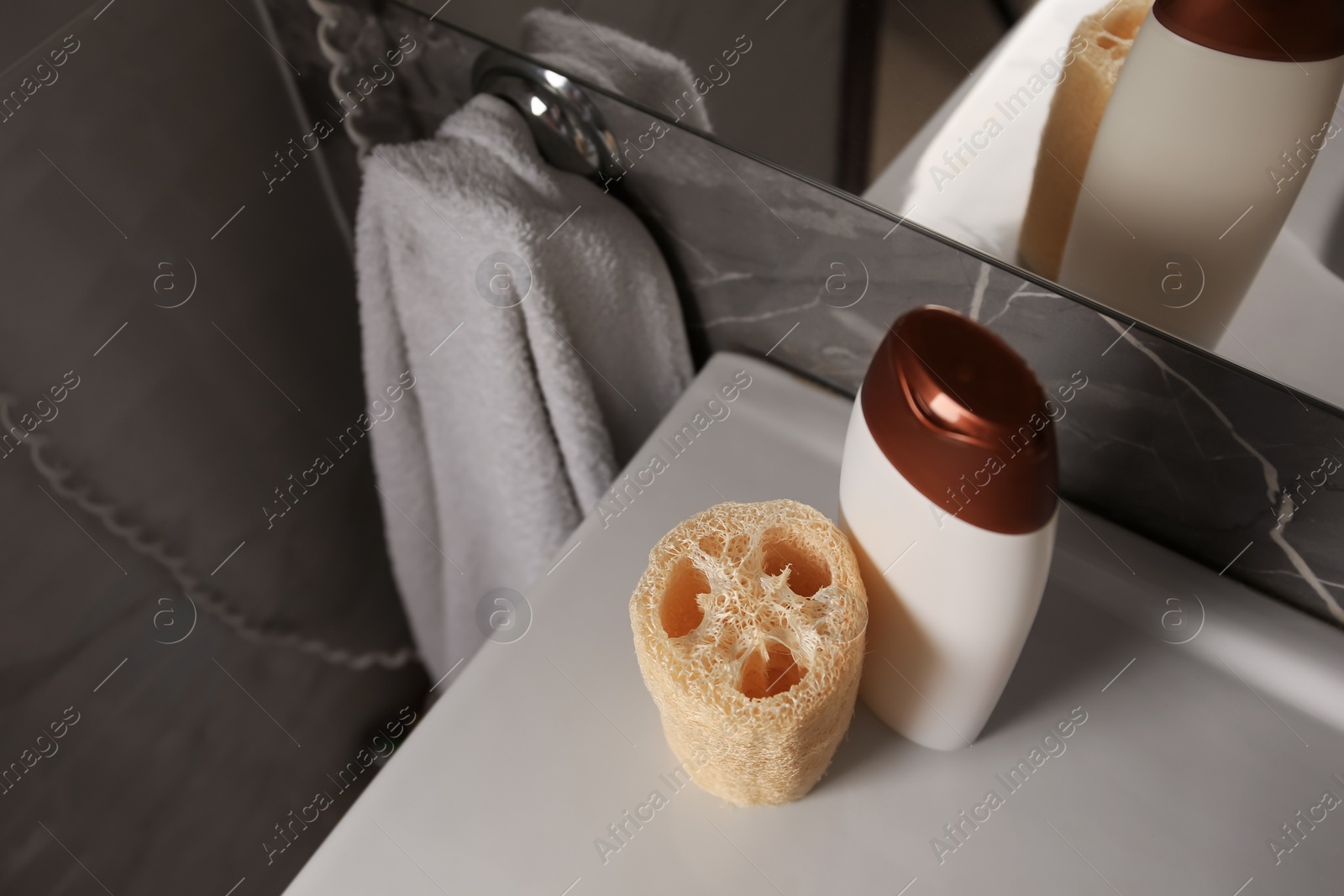 Photo of Natural loofah sponge and bottle with shower gel on washbasin in bathroom, above view