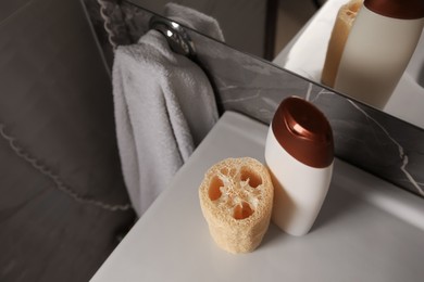 Natural loofah sponge and bottle with shower gel on washbasin in bathroom, above view