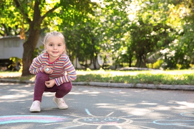 Photo of Little child drawing with colorful chalk on asphalt. Space for text