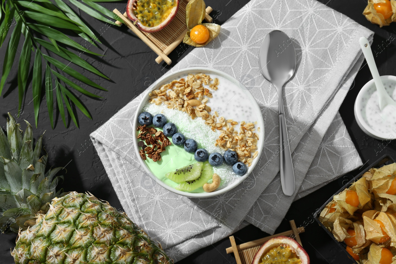 Photo of Tasty smoothie bowl with fresh kiwi fruit, blueberries and oatmeal served on black table, flat lay