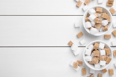 Photo of Different sugar cubes in bowls on white wooden table, flat lay. Space for text