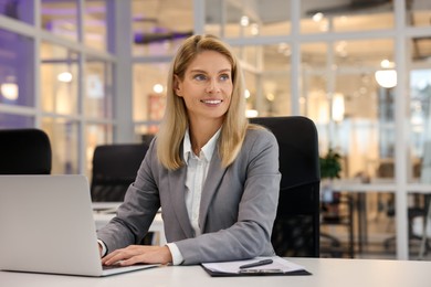 Photo of Smiling woman working with laptop at table in office. Lawyer, businesswoman, accountant or manager