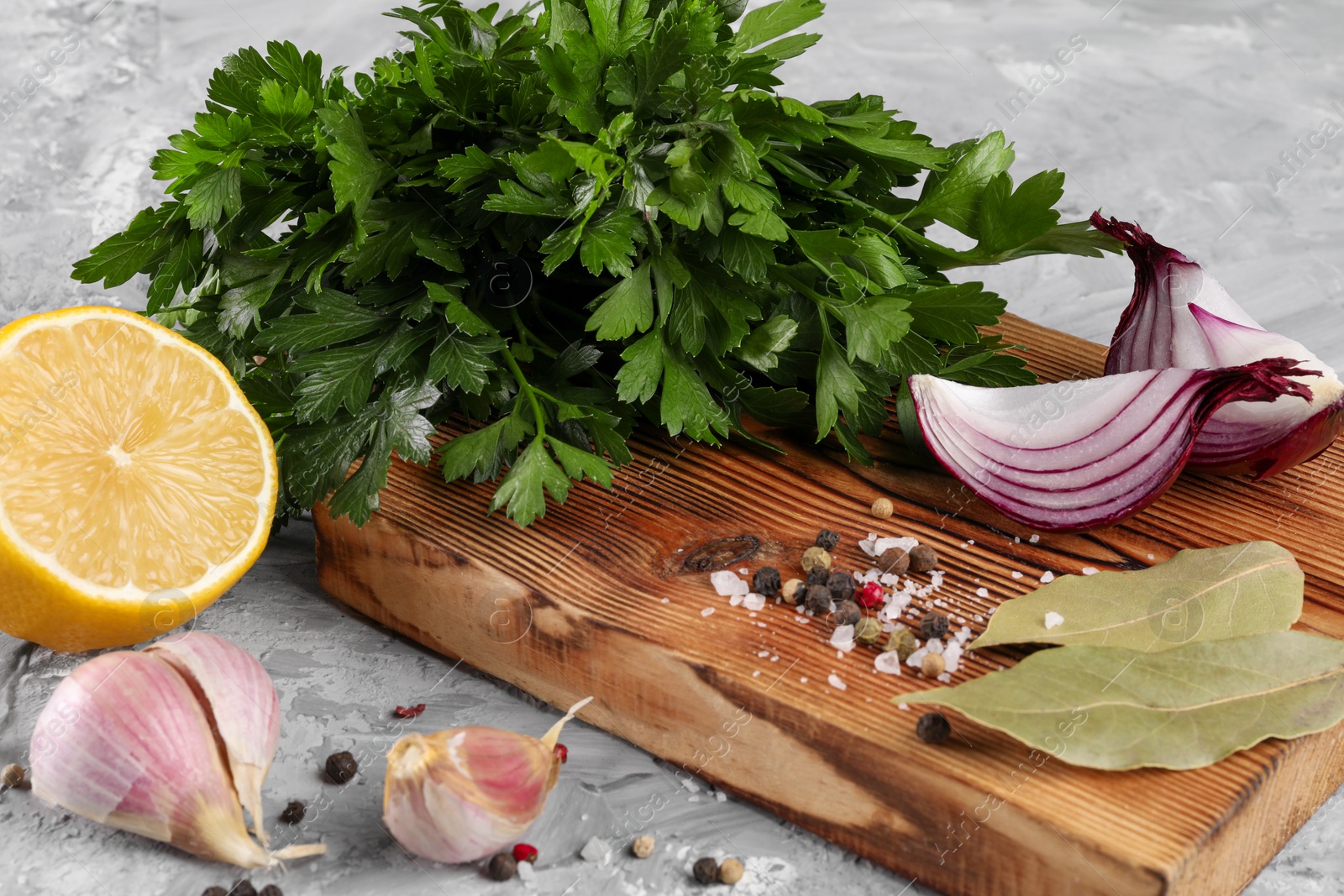 Photo of Bunch of fresh parsley, lemon, onion, garlic and spices on grey textured table