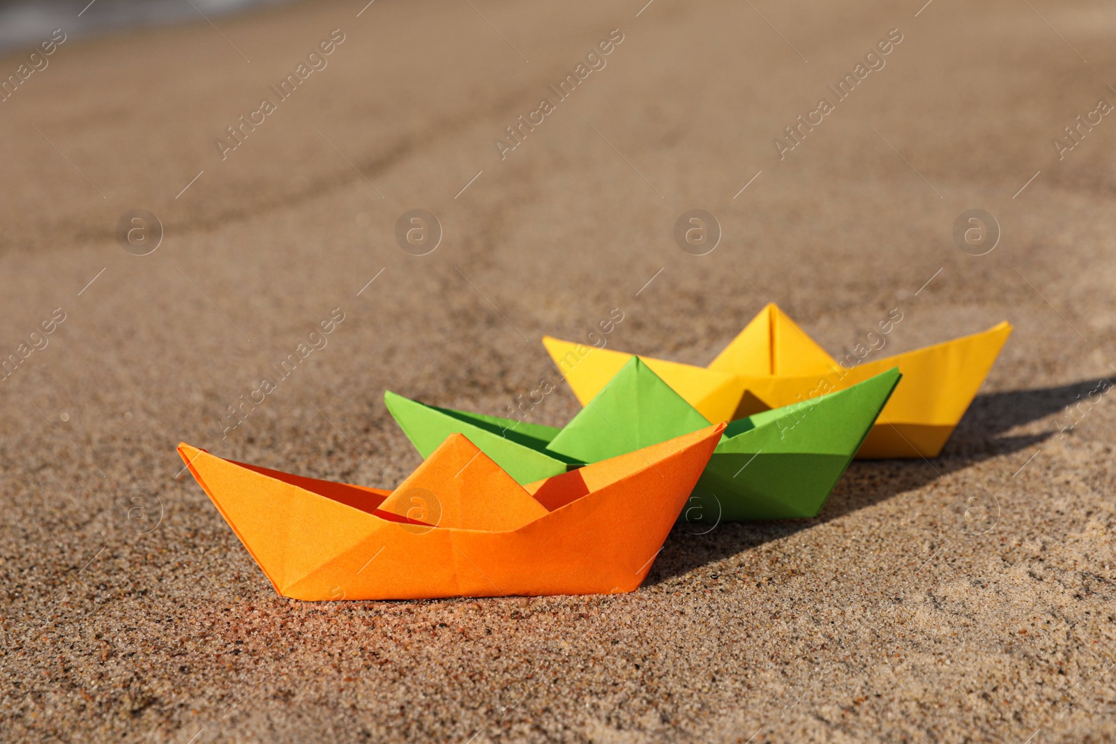 Photo of Bright color paper boats on sandy beach near sea