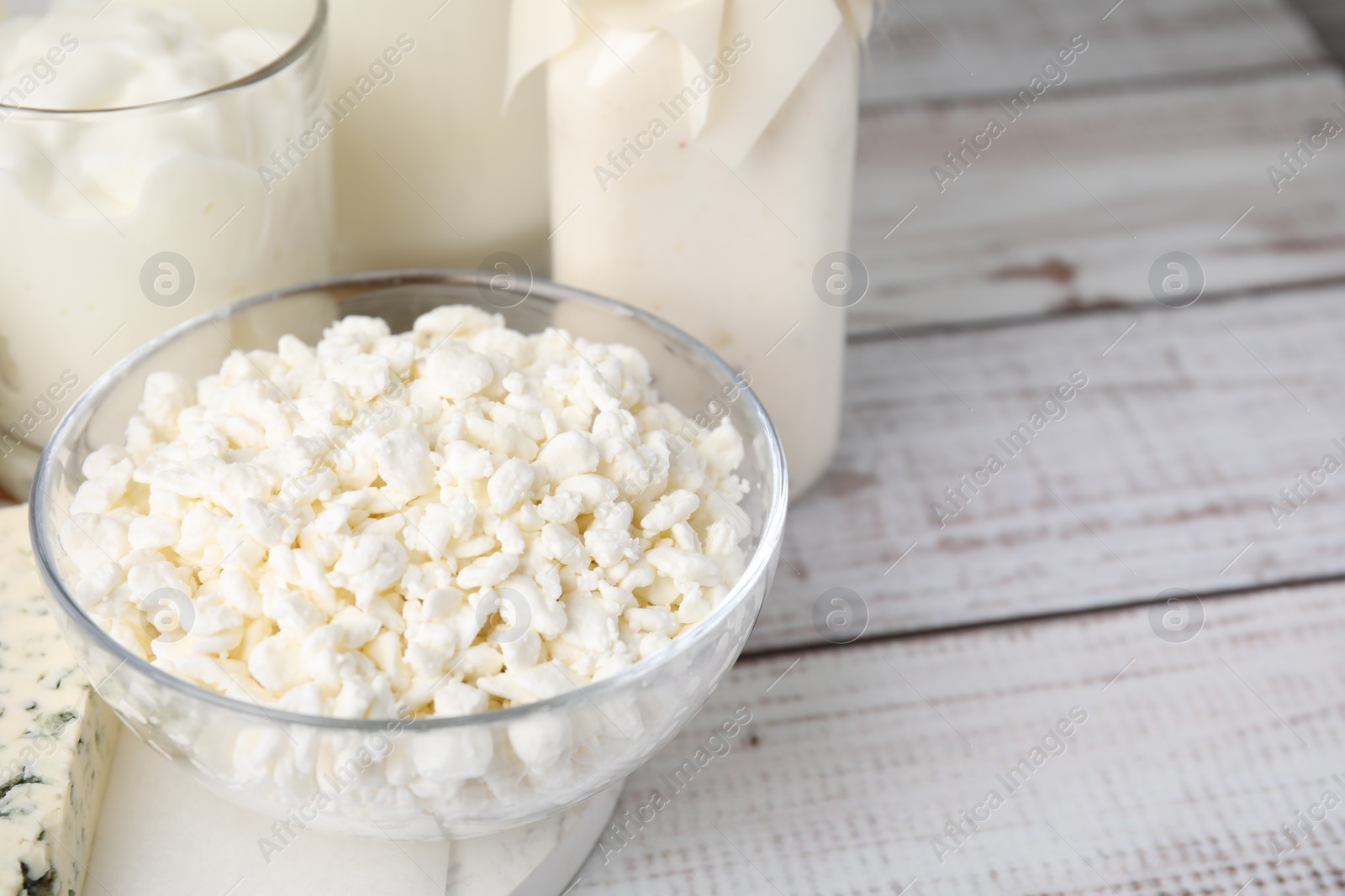 Photo of Tasty cottage cheese and other fresh dairy products on white wooden table, closeup. Space for text