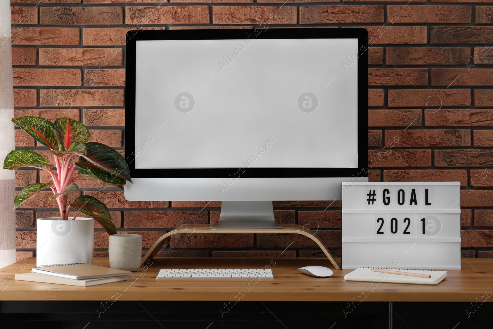 Photo of Light box with hashtag Goal 2021 near computer monitor on wooden desk in office