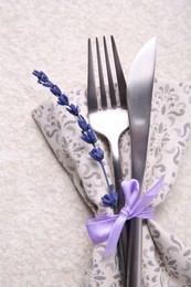 Cutlery, napkin and preserved lavender flower on white textured table, top view