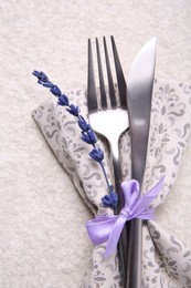 Photo of Cutlery, napkin and preserved lavender flower on white textured table, top view