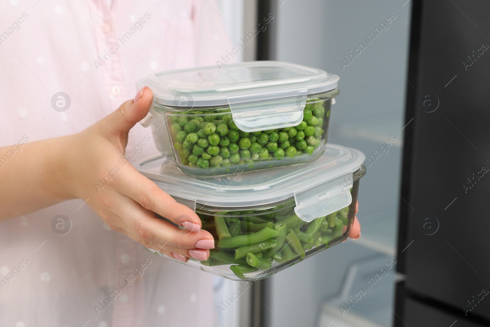 Photo of Woman holding containers with different fresh products near fridge, closeup. Food storage