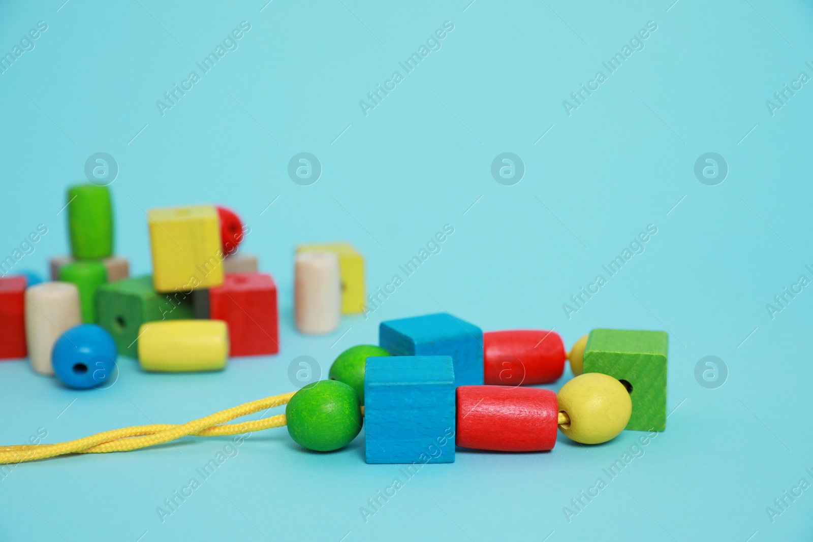 Photo of Wooden pieces and string for threading activity on light blue background, closeup. Educational toy for motor skills development