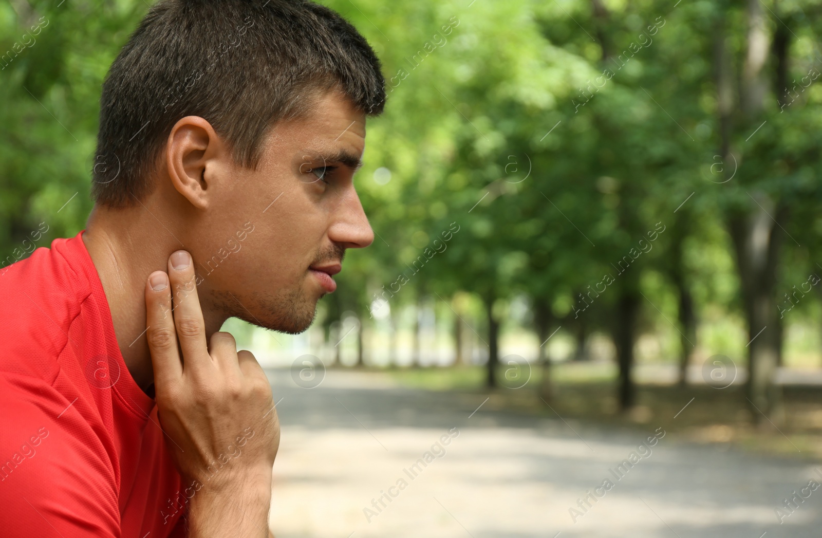 Photo of Young man checking pulse after training in park. Space for text