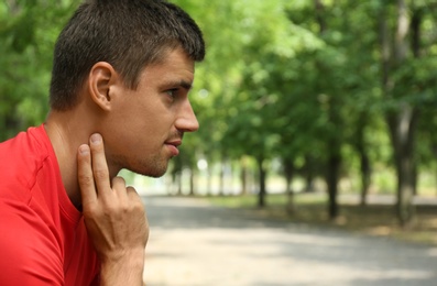Photo of Young man checking pulse after training in park. Space for text