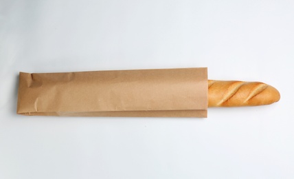 Photo of Paper bag with baguette on white background, top view. Space for design