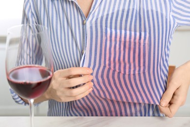 Photo of Woman with wine stain on her shirt at white marble table indoors, closeup