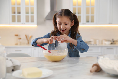 Photo of Cute little girl cooking dough at table in kitchen