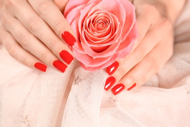 Woman holding manicured hands with red nail polish near rose on fabric, closeup