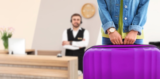 Image of Woman with suitcase near receptionist in hotel, closeup view