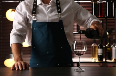 Bartender pouring red wine into glass at counter indoors, closeup