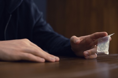 Criminal holding drug at table indoors, closeup