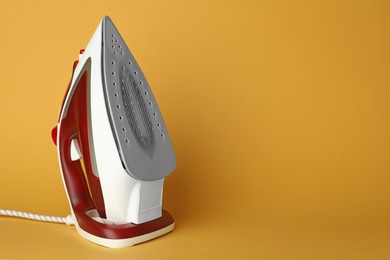 Photo of One modern iron on orange background, space for text. Home appliance