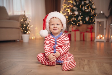 Photo of Cute baby in Christmas pajamas and Santa hat indoors