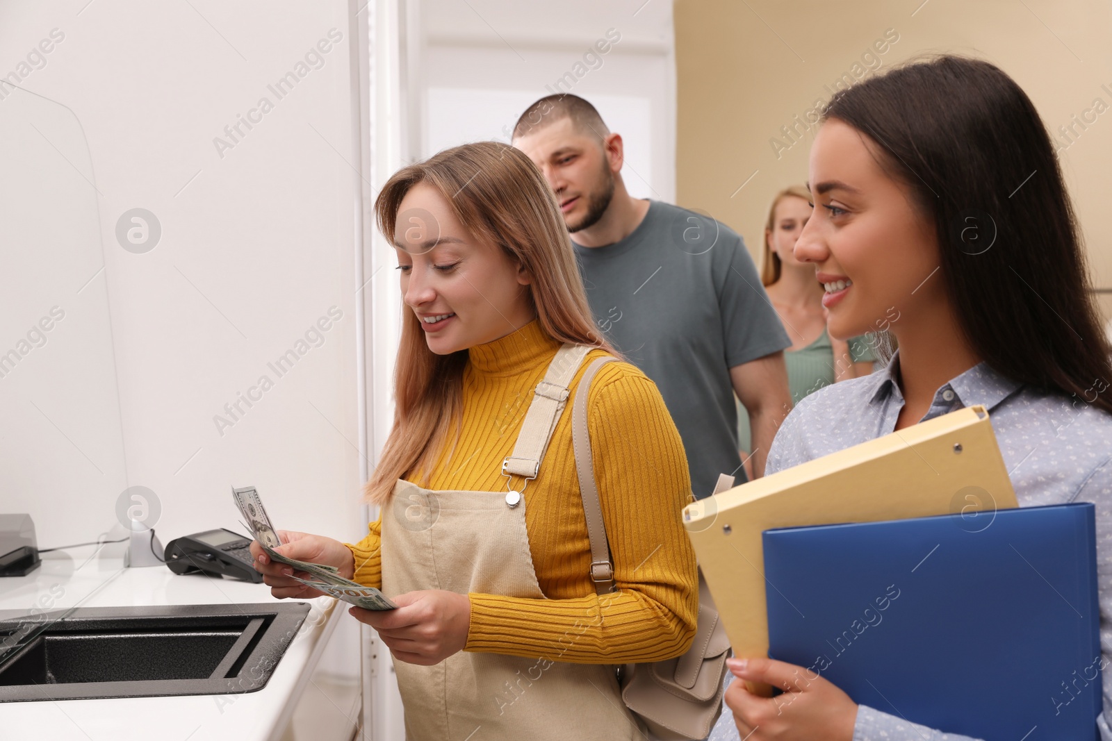 Photo of Woman with money and other people in line at cash department window. Currency exchange