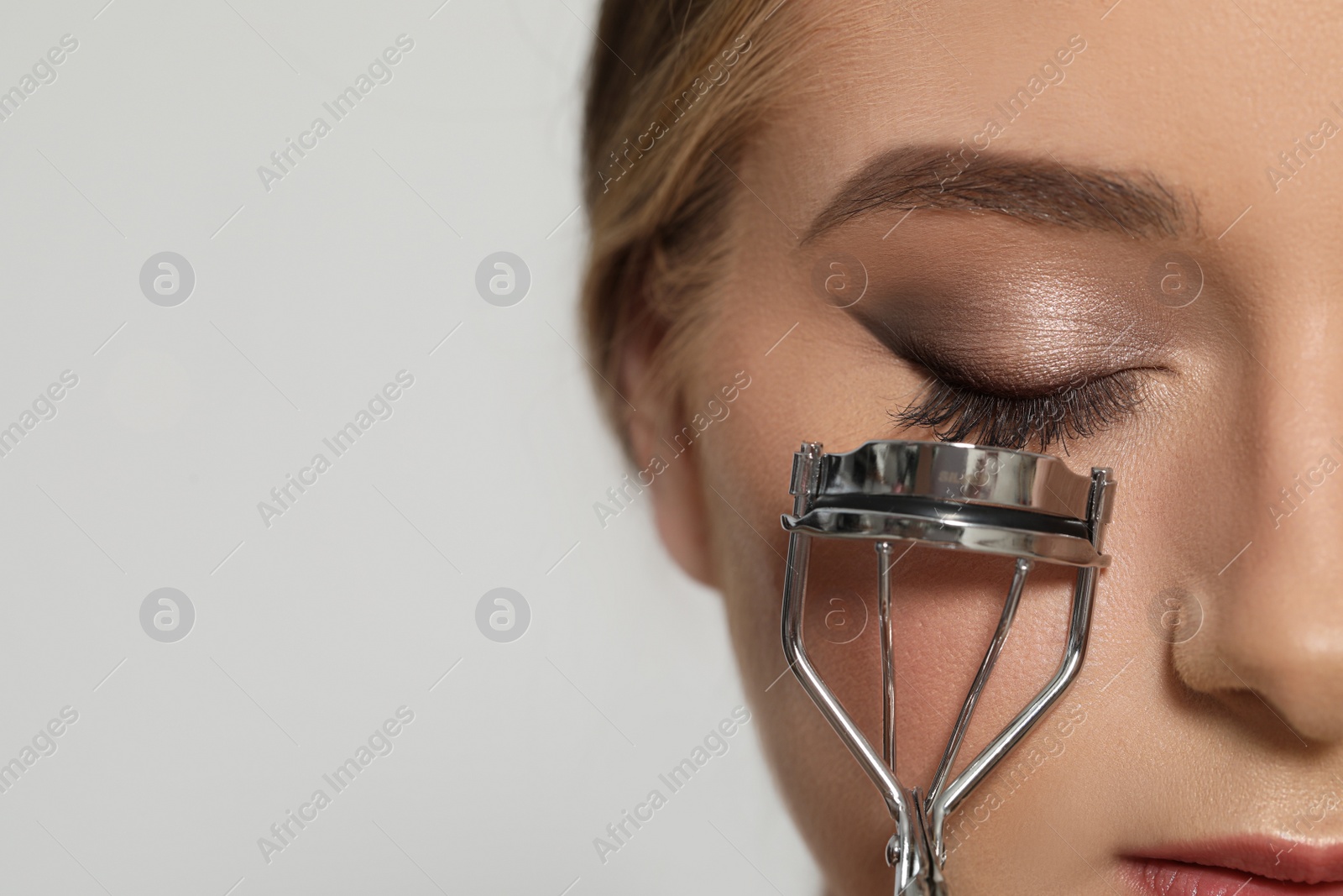 Photo of Young woman using eyelash curler on white background, closeup. Space for text