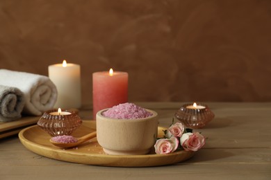 Photo of Bowl of pink sea salt, roses, burning candles, herbal massage bags and towels on wooden table