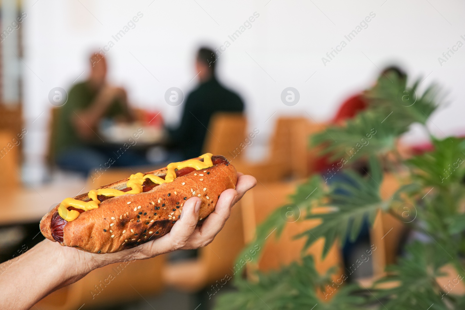 Photo of Woman holding fresh tasty hot dog with mustard in cafe, closeup. Space for text