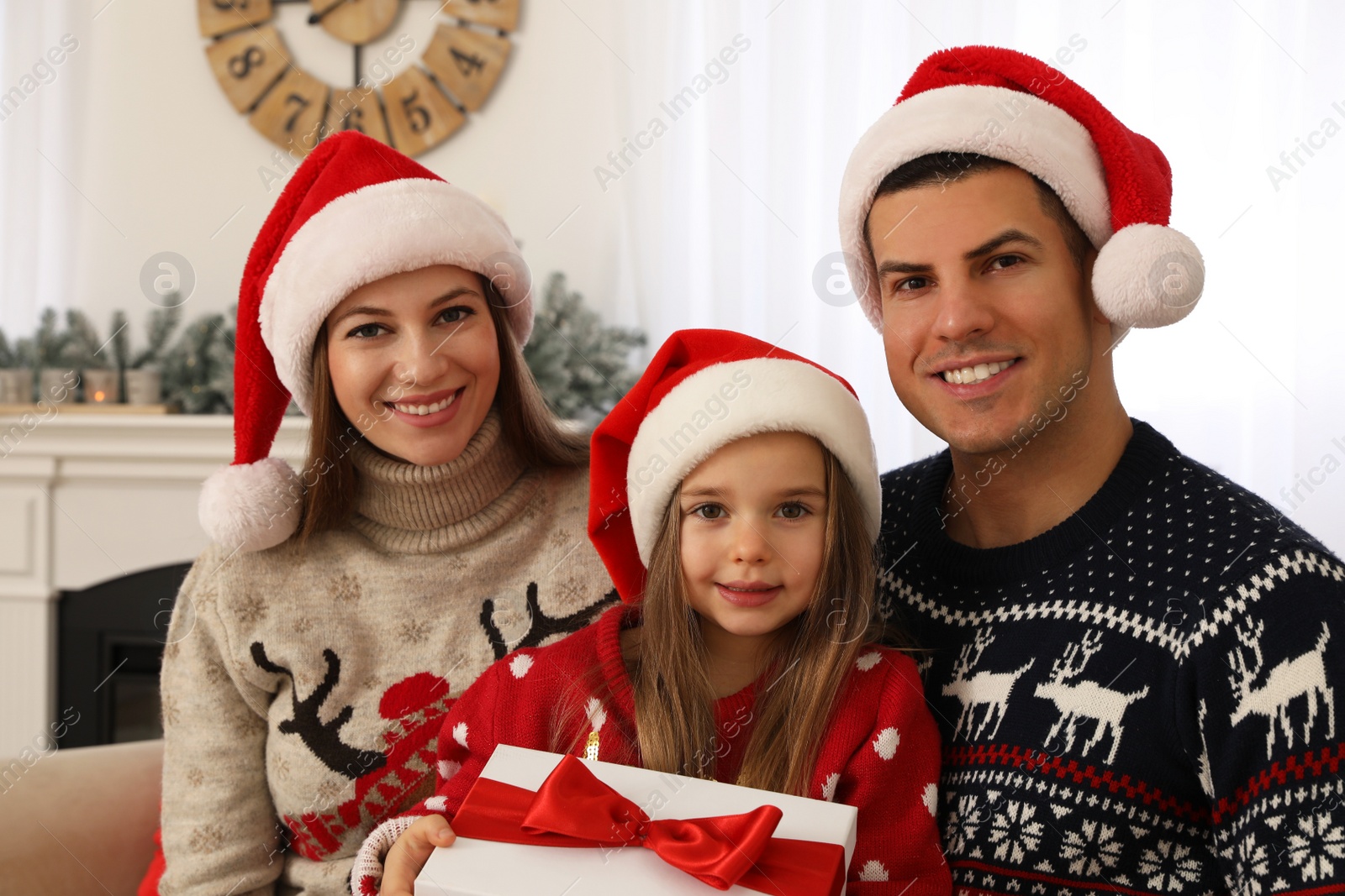 Photo of Happy family in Santa hats at home. Daughter holding Christmas present