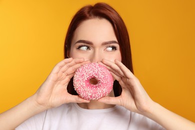 Photo of Beautiful redhead woman covering mouth with donut on orange background